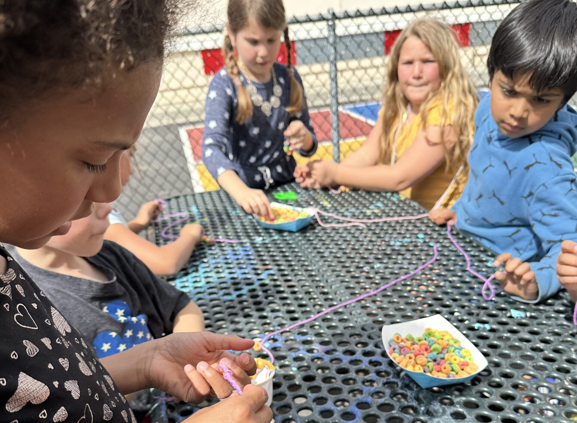 group of kids at a table making bracelets with fruit loops